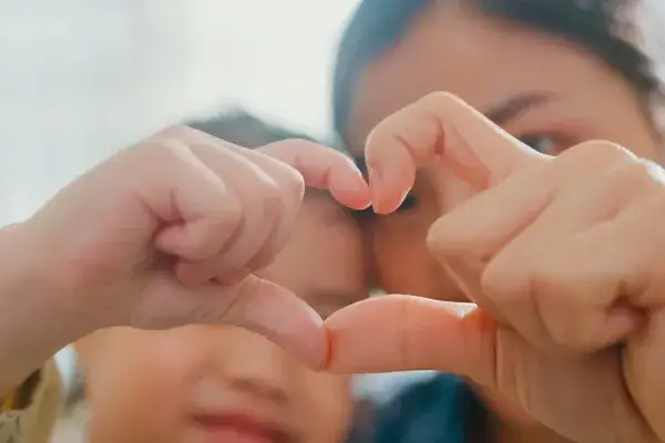 Closeup of young foster child making fingers heart shaped signs with foster aunt