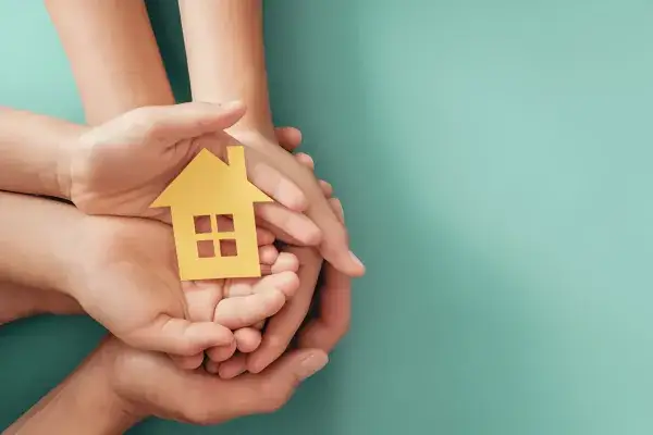 Hands holding yellow paper house on blue background, family home
