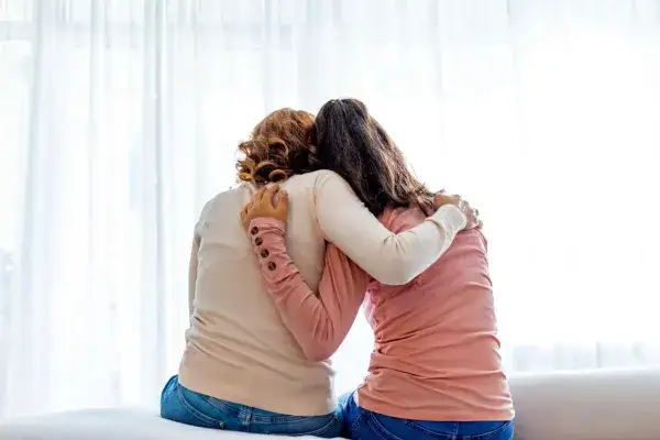 foster Mother with a foster teenager side hugging with backs facing camera.