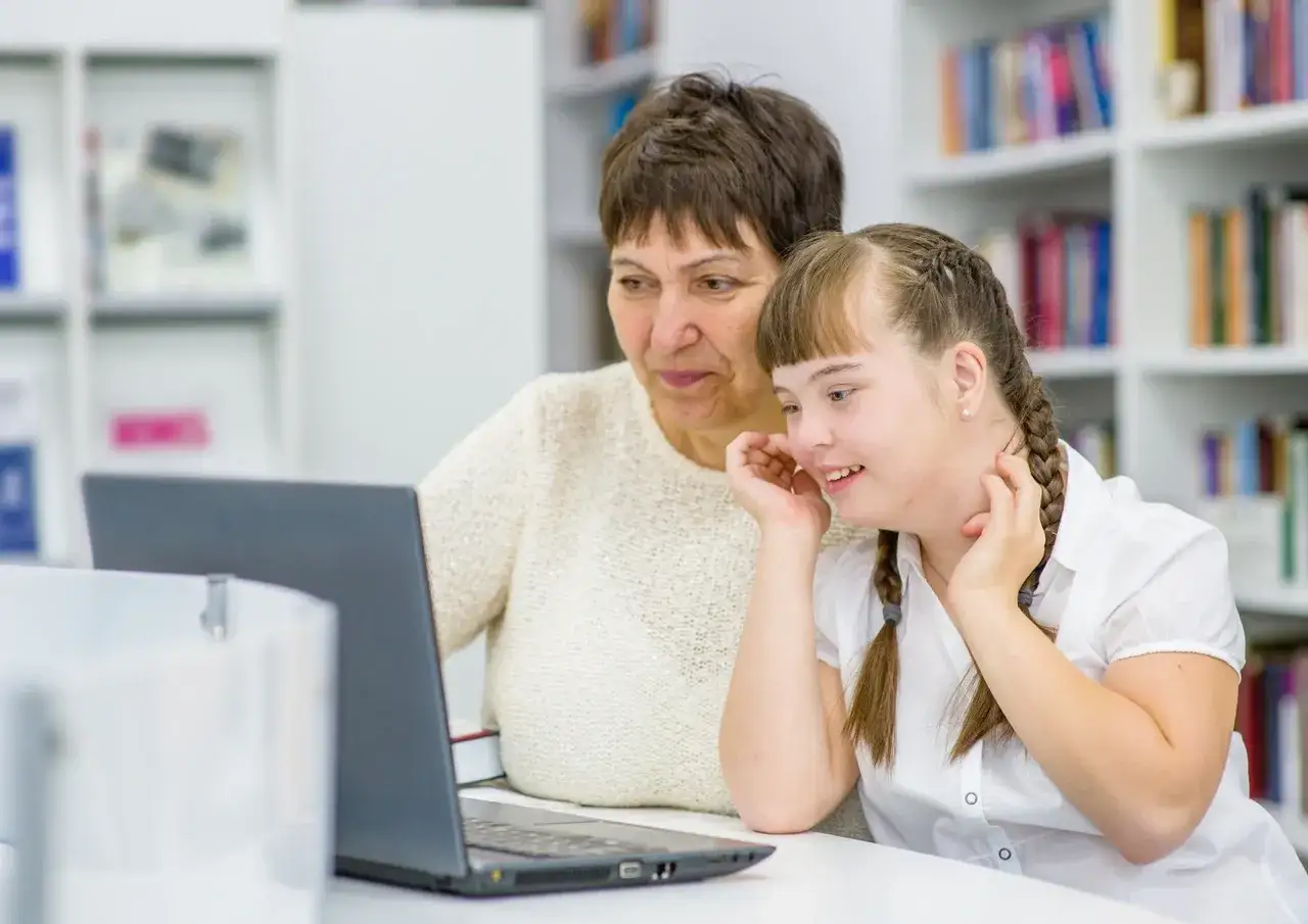 A Down syndrome girl with a foster mother looking at a laptop