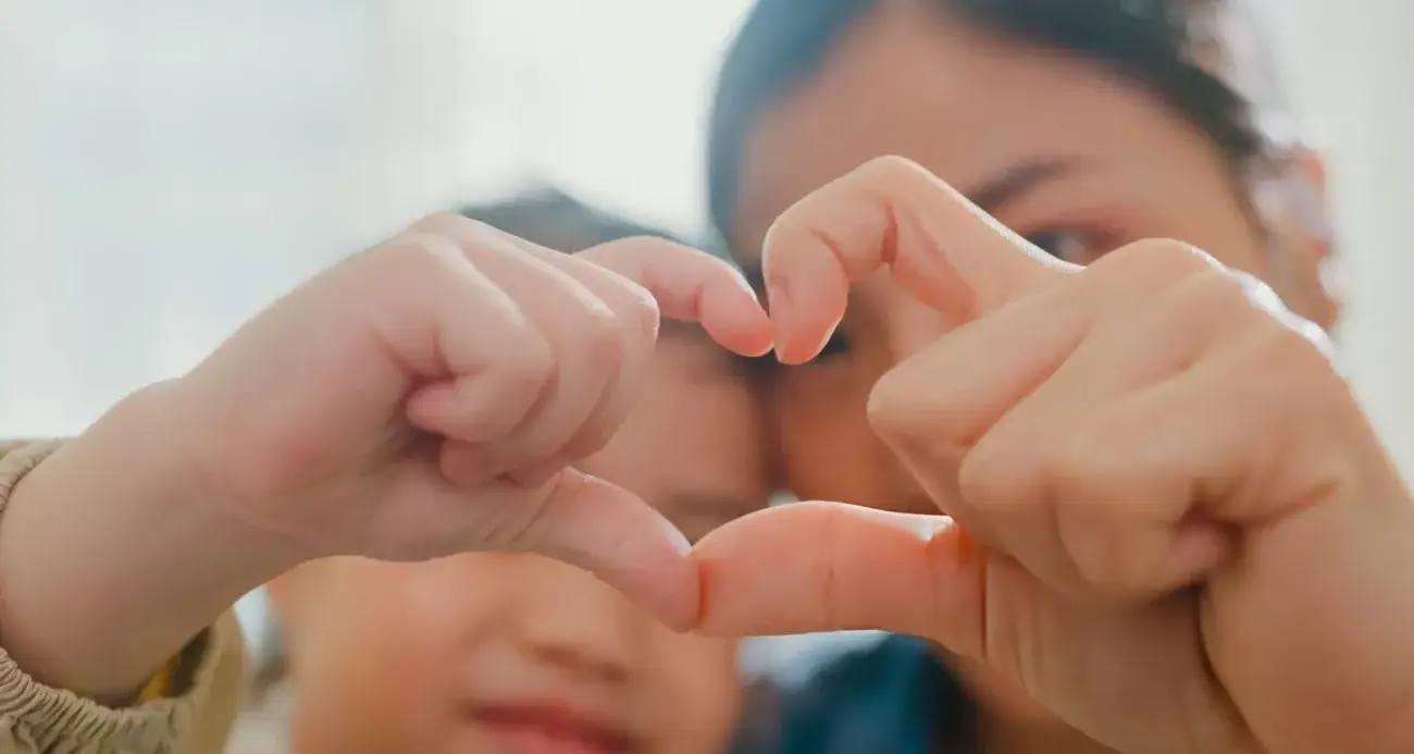 Closeup of young foster child making fingers heart shaped signs with foster aunt