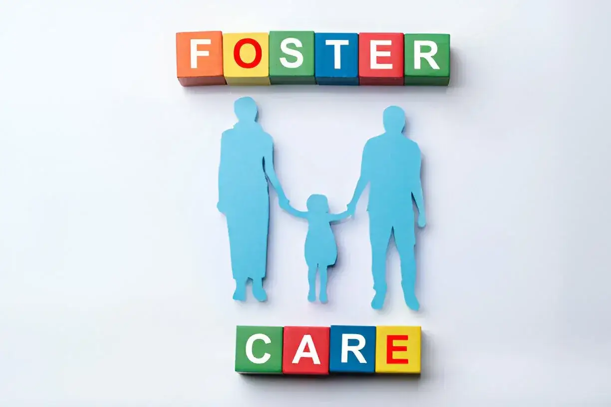 Foster care written in colorful wooden blocks a paper cut out of a family.