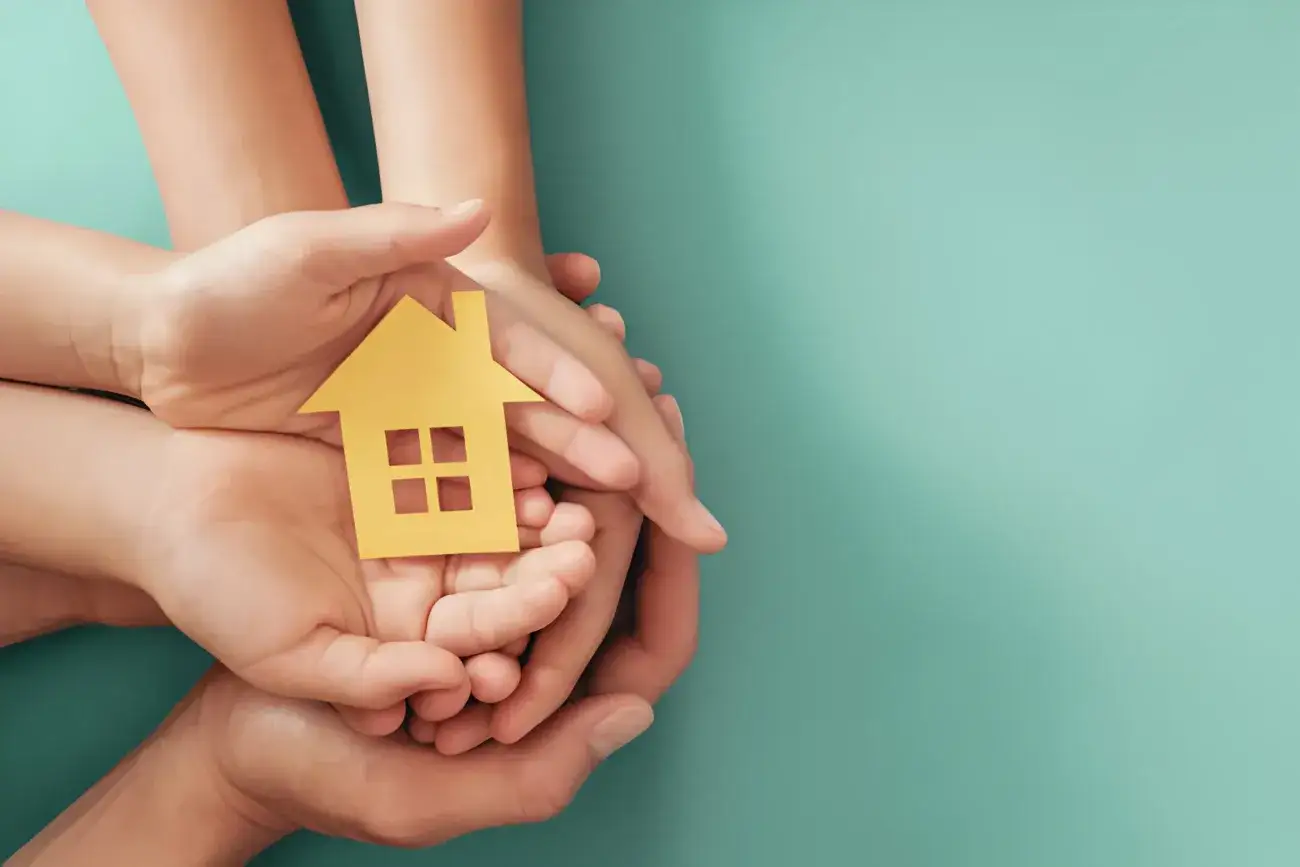 Hands holding yellow paper house on blue background, family home