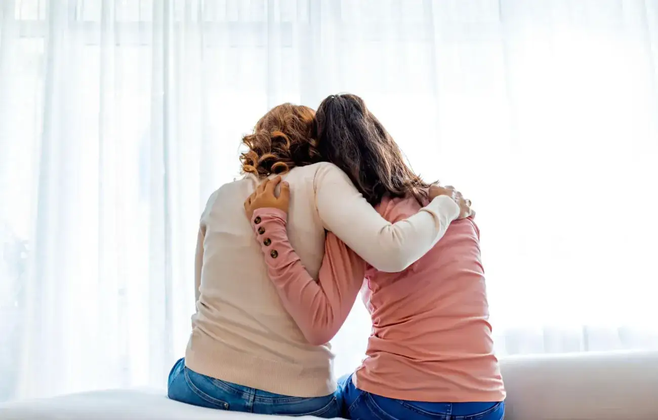 foster Mother with a foster teenager side hugging with backs facing camera.