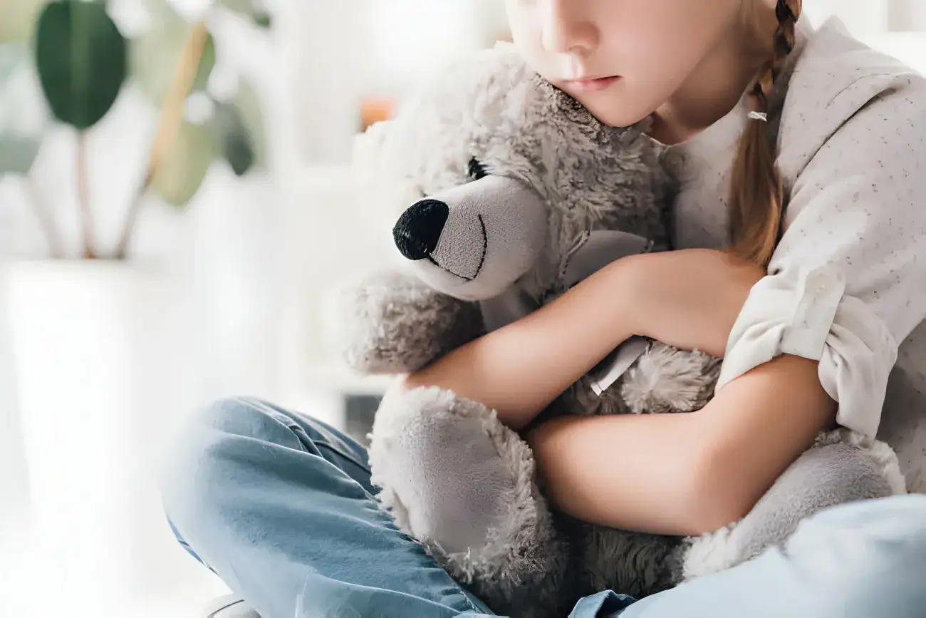 shot of depressed young foster child embracing her teddy bear